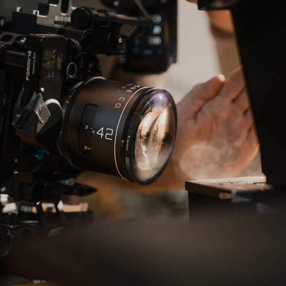 Close-up of a professional film camera lens with a hand adjusting equipment in the background.