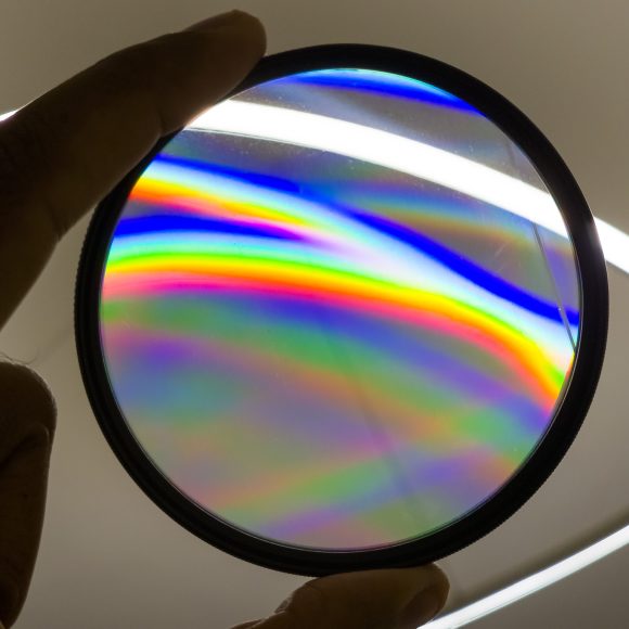 SZ Filters - Rainbow Starlight & Blast Make In-Camera Magic A hand holds a circular glass filter showing rainbow-colored light patterns against a white background.