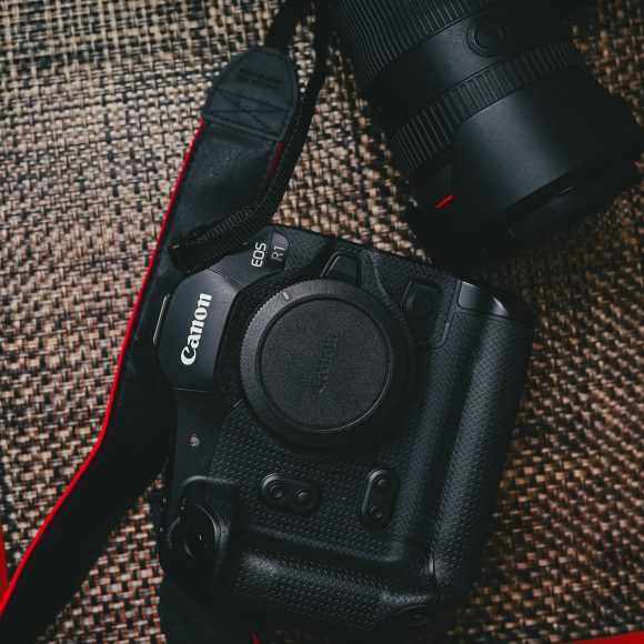 Canon EOS R1 camera with lens and cup of coffee on a woven mat.