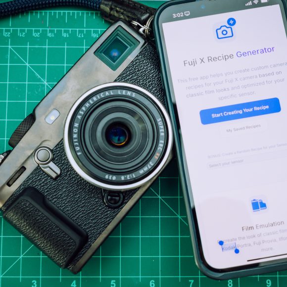 A camera and a smartphone displaying a Fuji X Recipe Generator page on a green cutting mat.