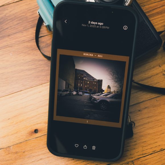 A smartphone on a wooden surface displays a photo of parked cars beside a brick building.
