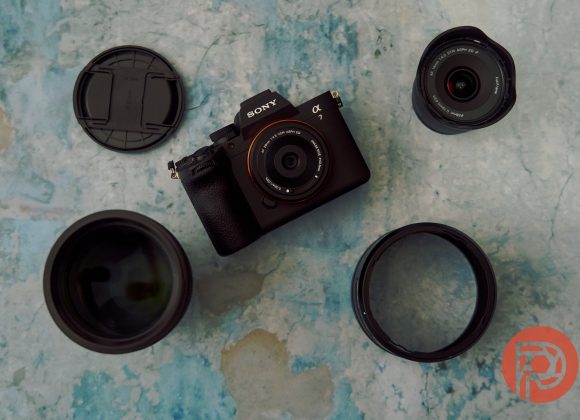 Chinese Lenses Aren't Cheap. We're Just Used to Overpaying Sony camera and three lenses arranged on a blue surface, with lens caps nearby and a red logo in the corner.