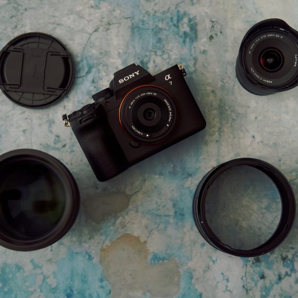 Sony camera and three lenses arranged on a blue surface, with lens caps nearby and a red logo in the corner.