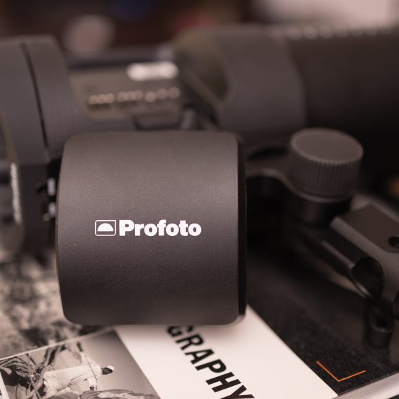 Close-up of a Profoto camera flash unit resting on top of books and magazines.
