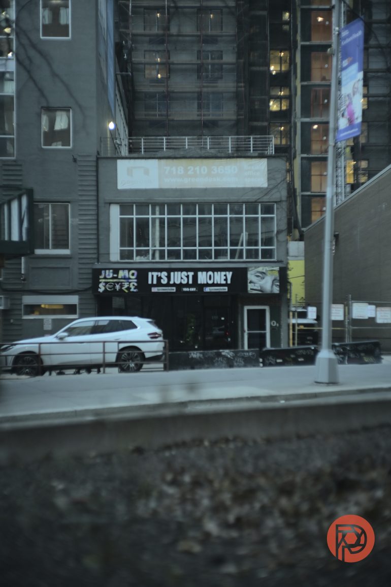 A city street view with a building sign that reads ITS JUST MONEY above a white SUV.