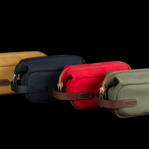 Four small zippered bags in yellow, black, red, and green, each with a brown leather strap, on a black background.