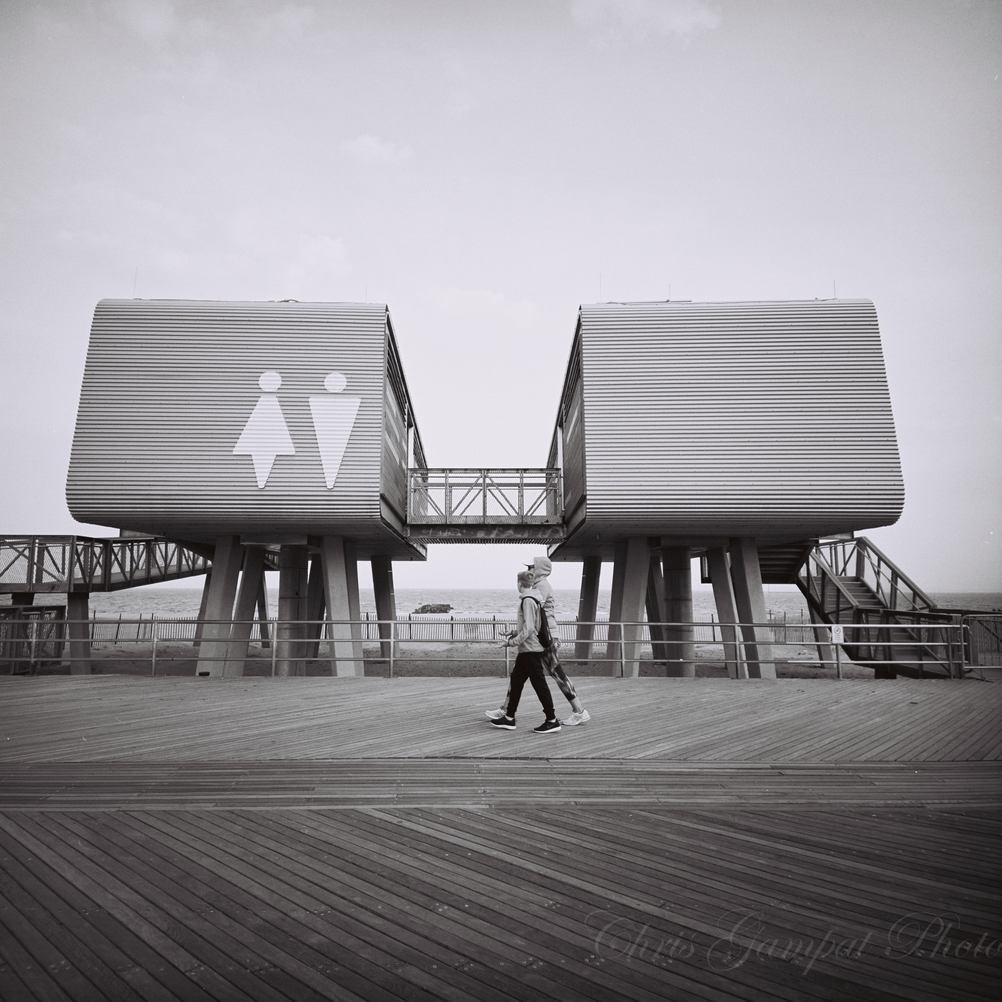 A person walks past two modern restroom buildings with large male and female symbols on the facade.