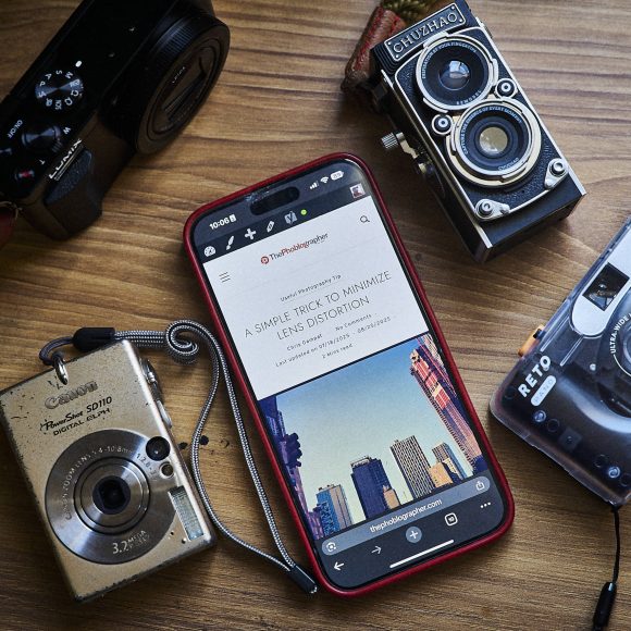 A smartphone and four vintage cameras are arranged on a wooden surface.