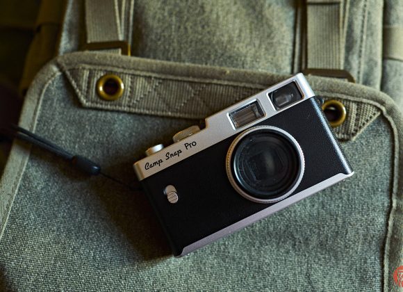 The Rise of the American Camera Brand A vintage black camera labeled Camp Snap Pro rests on a green canvas backpack.