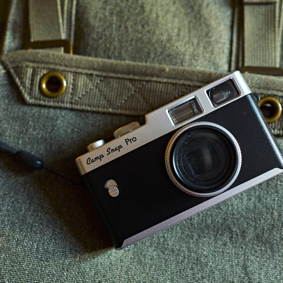 A vintage black camera labeled Camp Snap Pro rests on a green canvas backpack.