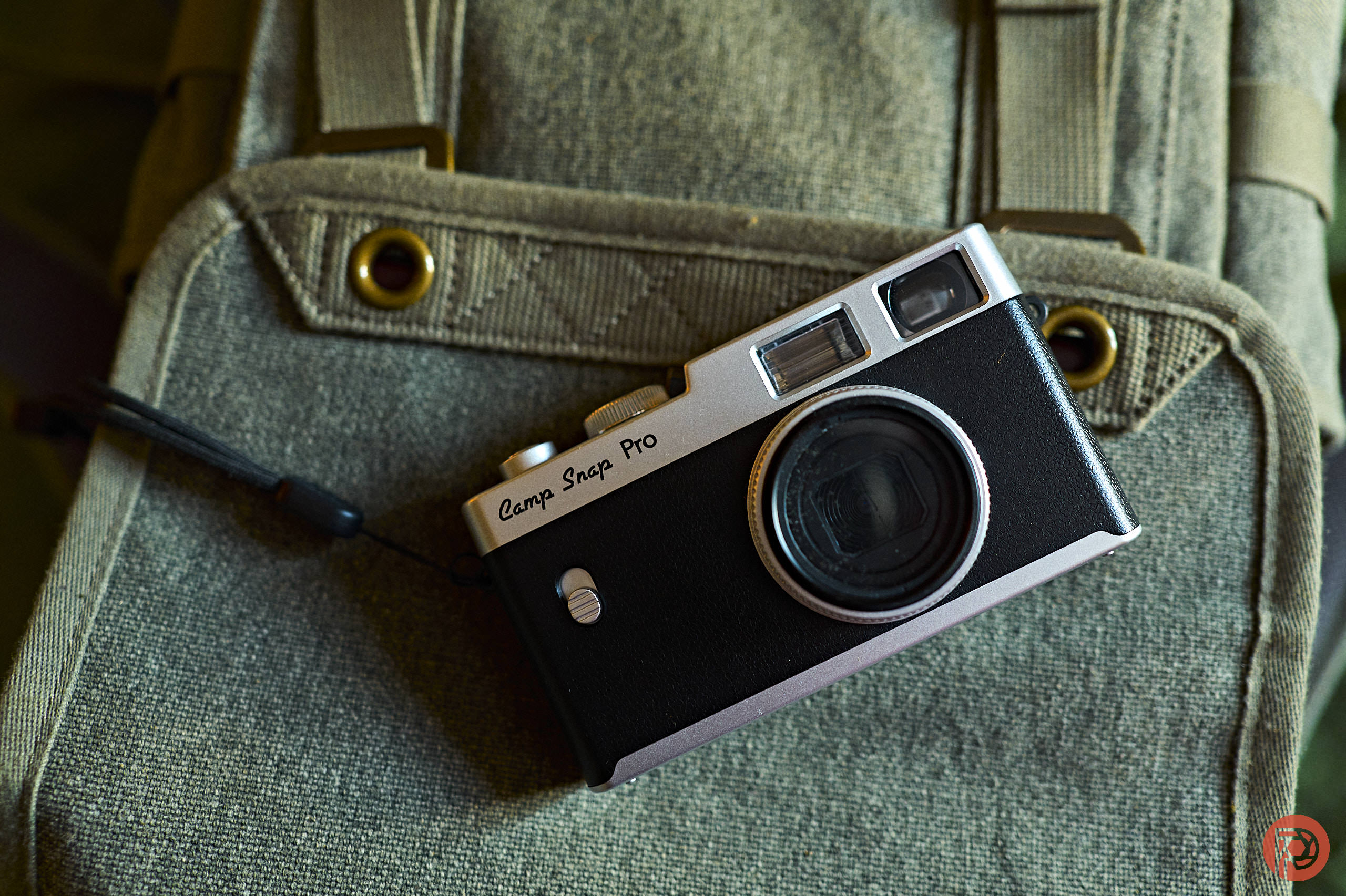 The Rise of the American Camera Brand A vintage black camera labeled Camp Snap Pro rests on a green canvas backpack.