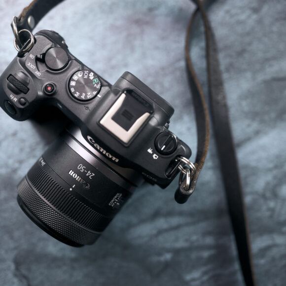 A Canon mirrorless camera with a zoom lens and strap resting on a textured blue surface.