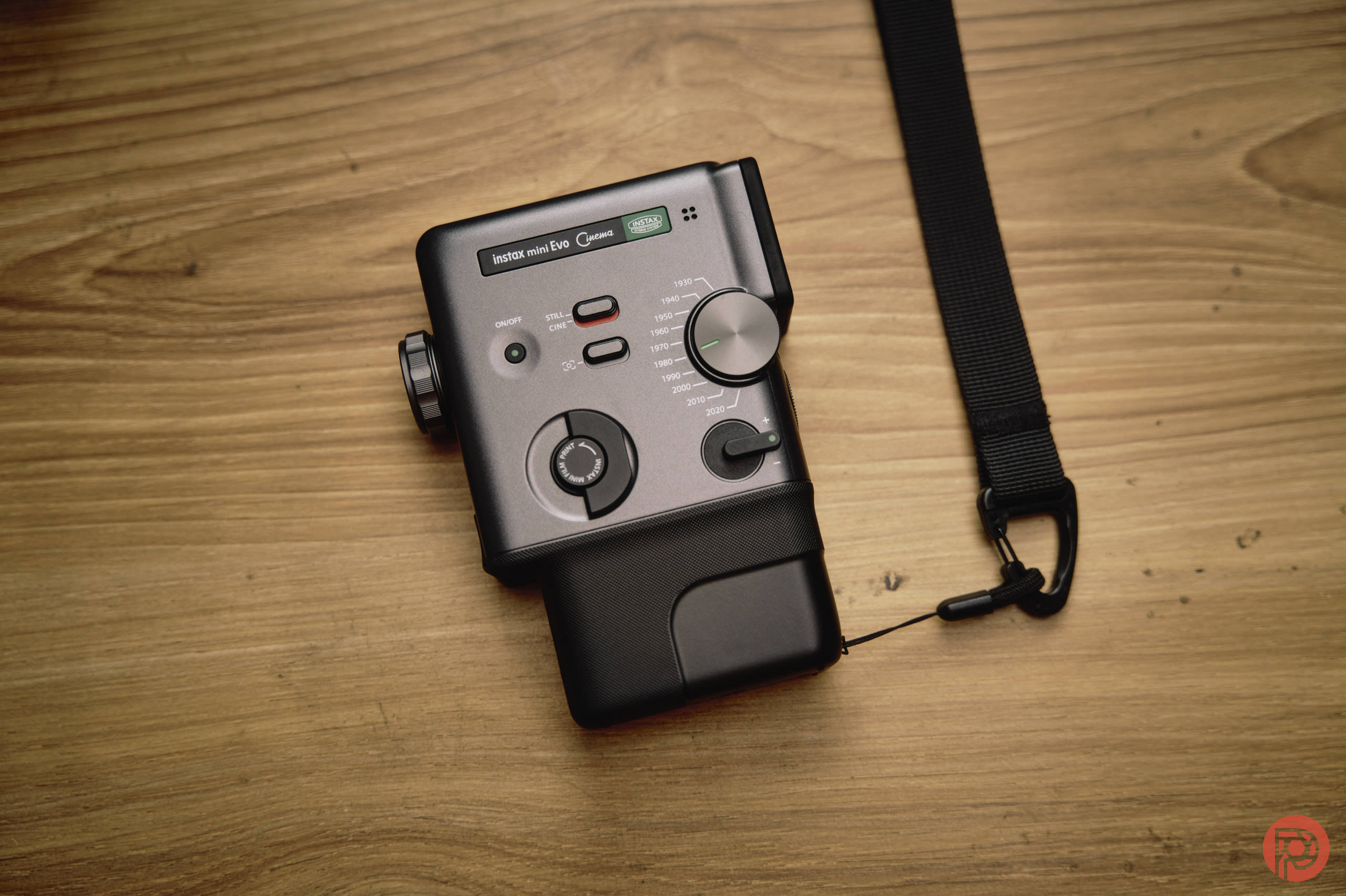 A black handheld electronic device with dials and buttons on a wooden surface, attached to a black strap.