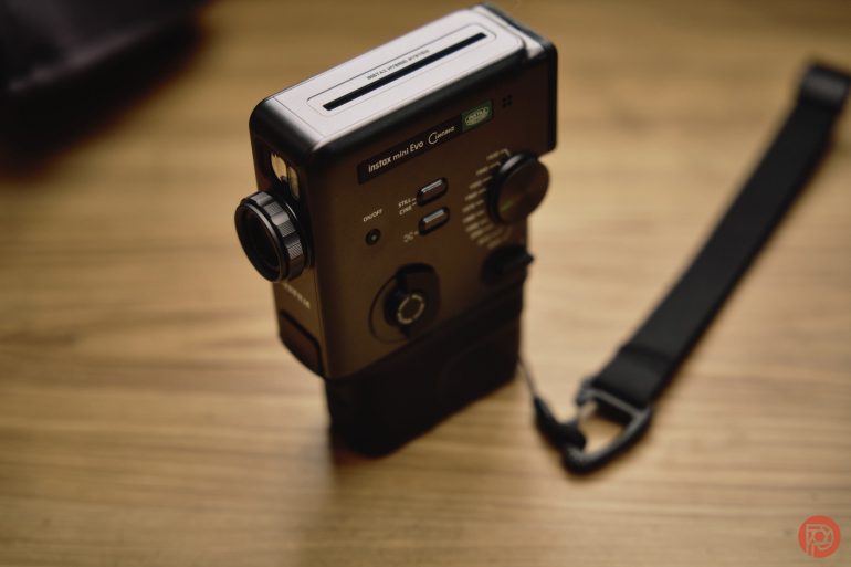 A vintage handheld camera with a wrist strap resting on a wooden surface.