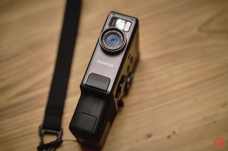 A Fujifilm camera with a black strap rests on a wooden surface.