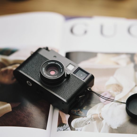 A black camera with a lens cap sits on an open fashion magazine featuring images of models in stylish outfits.