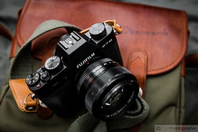 A Fujifilm X-T10 camera with a strap rests on a green and brown leather Oberwerth camera bag.