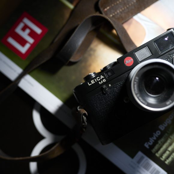 A Leica M6 camera with a strap sits on top of two photography magazines, one labeled LFI.