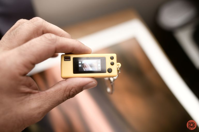 A hand holding a small yellow digital camera with its screen displaying a photo preview.