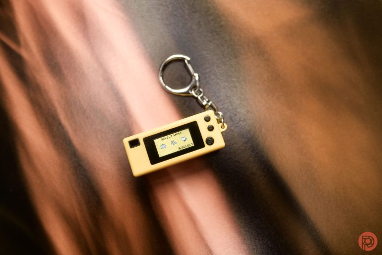 A small rectangular keychain with a screen and buttons, placed on a brown and black gradient surface.