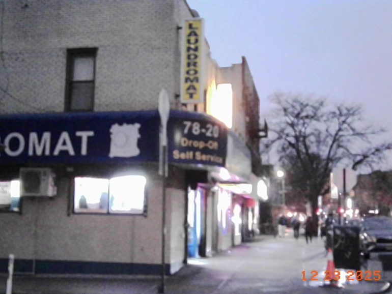 A laundromat with a blue sign and people walking on the sidewalk in the evening.