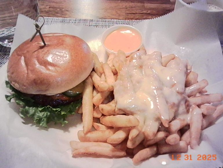 Burger with lettuce and pickles, served with cheese-covered fries and dipping sauce on a tray.