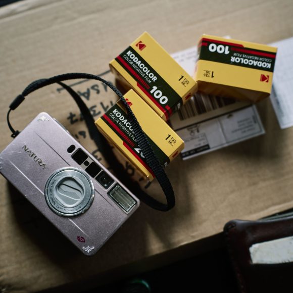 A vintage camera and three Kodak film boxes rest on a cardboard package.