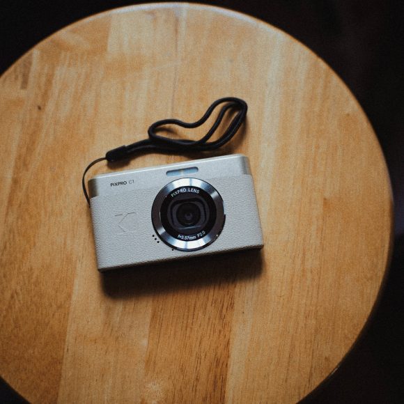 A silver digital camera with a wrist strap sits on a round wooden table.