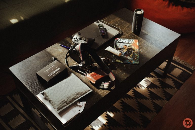 A cluttered coffee table with gadgets, keys, comics, a drink can, and other miscellaneous items.