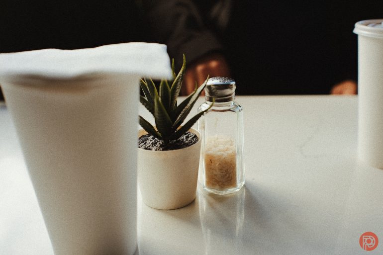 A small potted plant and a salt shaker on a white table, with cups on either side.