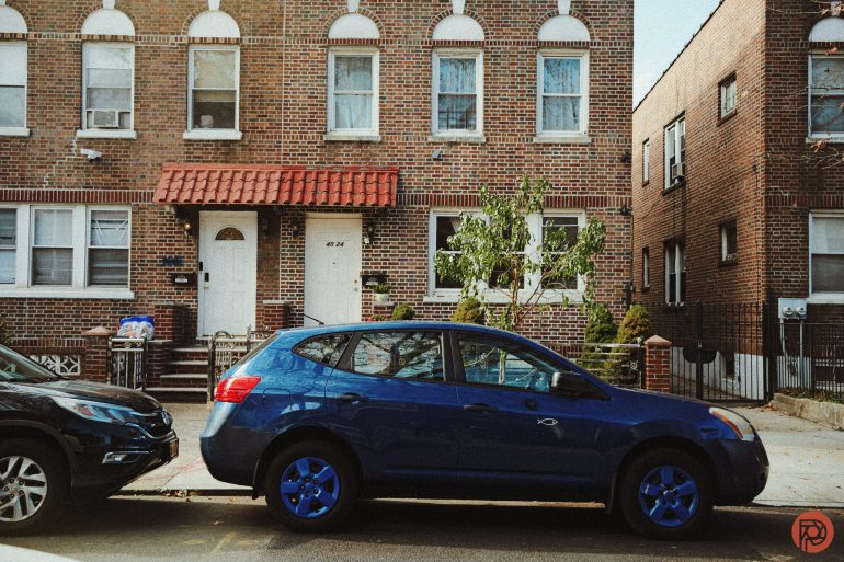 A blue car with painted wheels parked on a street in front of a brick apartment building.