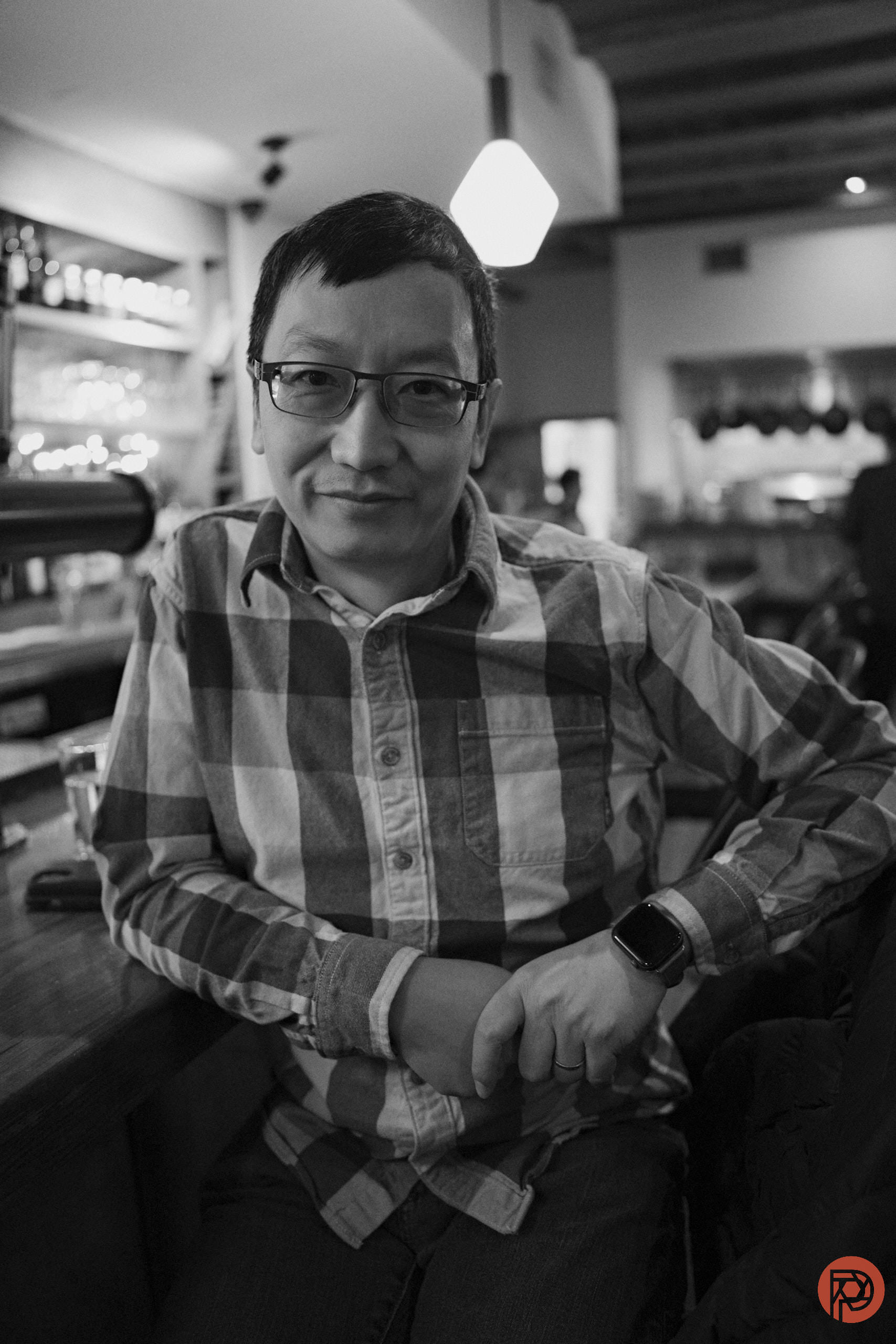 What are the Best Lenses for Black and White Photography? A person in glasses sits at a bar, smiling, in a black and white photo with a relaxed atmosphere.