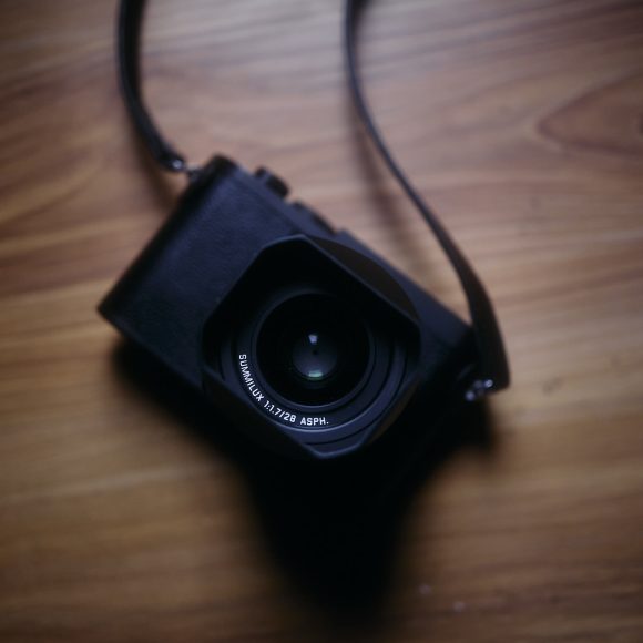 A black camera with a strap placed on a wooden surface, seen from above.