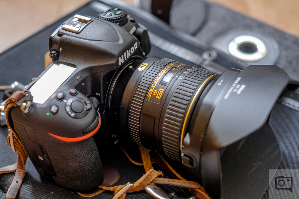 A Nikon DSLR camera with a wide lens and lens hood resting on a black surface.