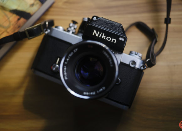 Vintage Nikon film camera with a lens and strap, placed on a wooden surface near a book or map.