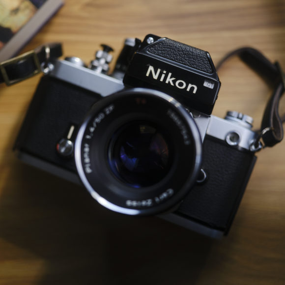 Vintage Nikon film camera with a lens and strap, placed on a wooden surface near a book or map.