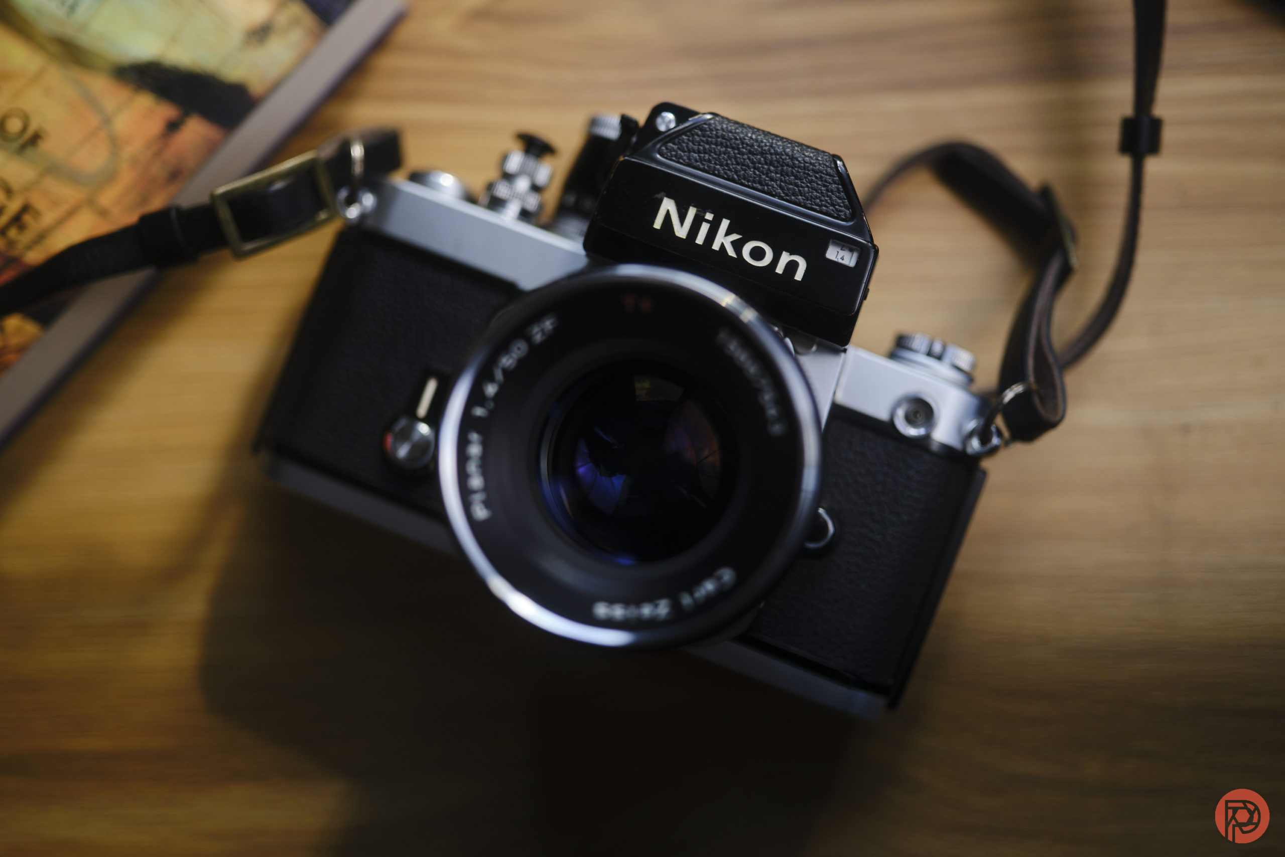 PSA: Your Camera's Shutter is Fine. Stop Worrying Vintage Nikon film camera with a lens and strap, placed on a wooden surface near a book or map.