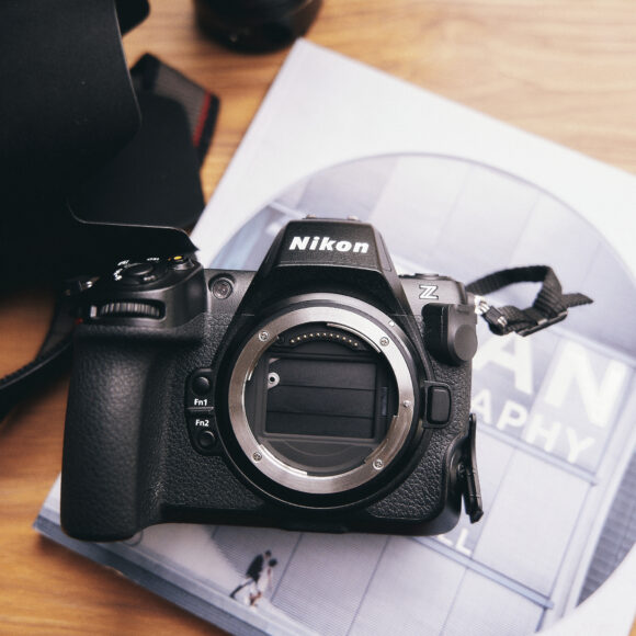 Nikon camera body on a book with a lens nearby, placed on a wooden surface.