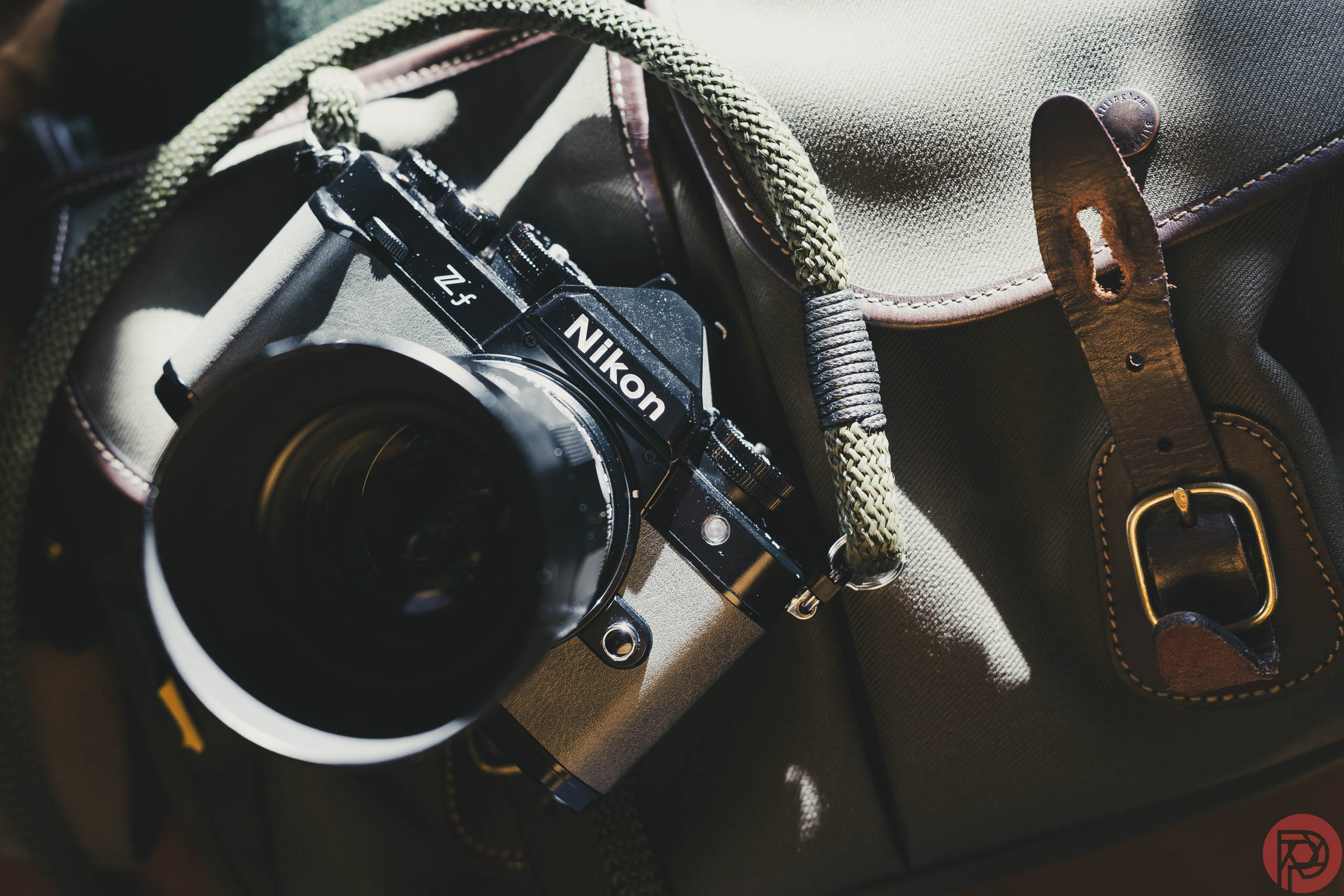 Why Photography Makes for Such a Great Solo Hobby A Nikon ZF camera with a green strap rests on a brown bag with leather buckle details.