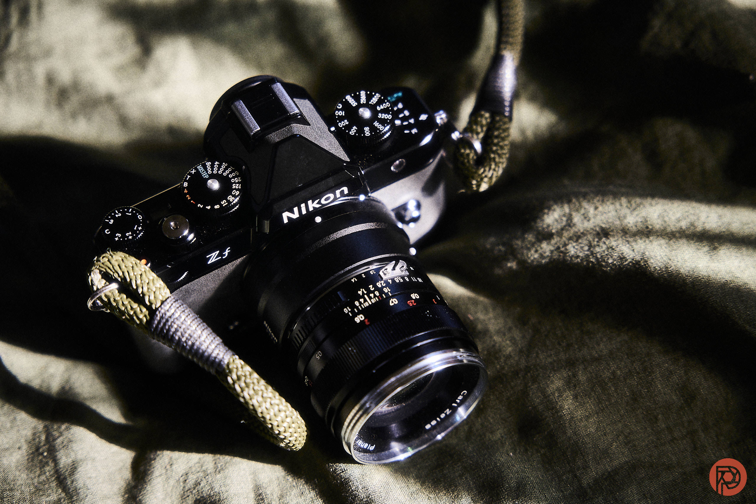 A Nikon Zf camera with a lens and strap lies on a textured green fabric.