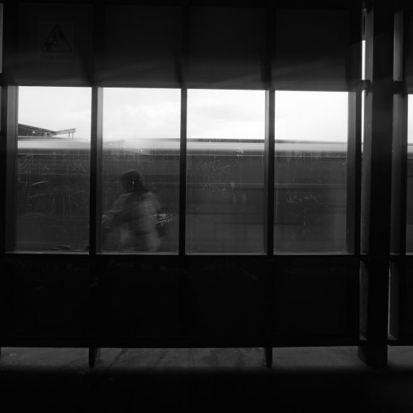 Silhouette of a person walking past train windows, black and white setting, with blurred train in motion.