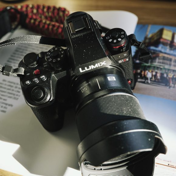 A Lumix S1R camera rests on an open magazine with photos of buildings and people.
