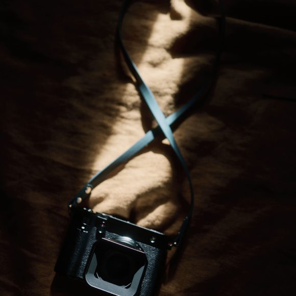 A black camera with a strap lying on a brown fabric, illuminated by a beam of sunlight.