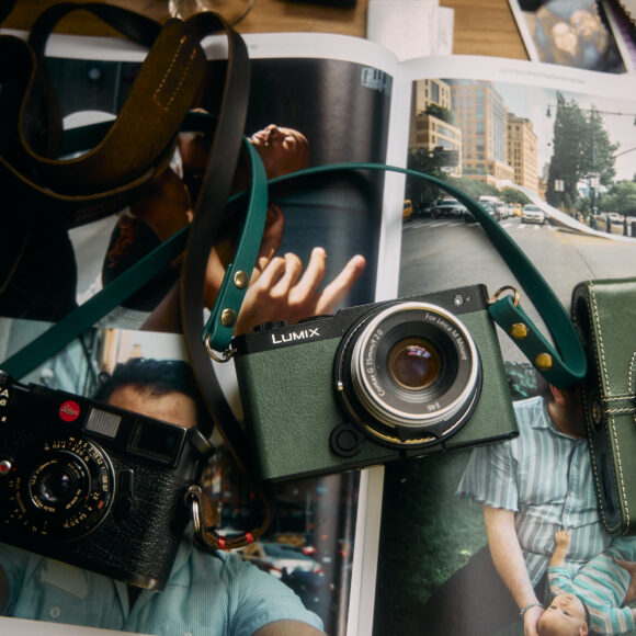 On a wooden table, three cameras with straps rest over an open magazine showcasing stunning photographs. Among them sits the sleek Panasonic S9, ready to capture the world in all its vibrant detail.