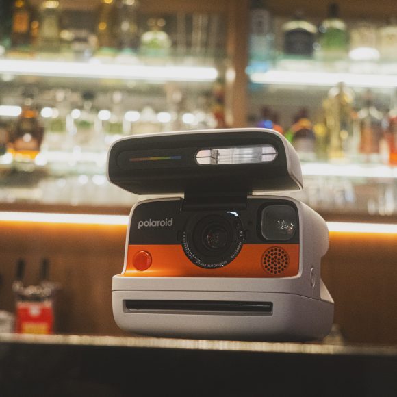 Polaroid camera on a dimly lit bar counter with blurred bottles in the background.