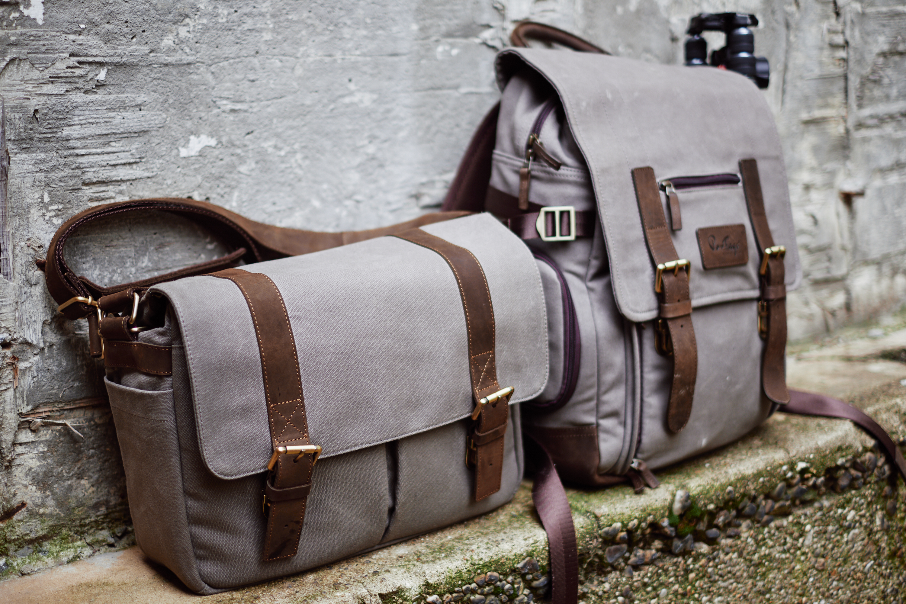 Two brown canvas bags with leather straps rest against a textured concrete wall, with a camera behind one bag.