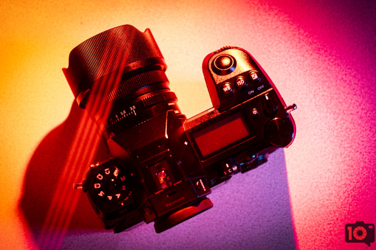 A black DSLR camera on a colorful, pink and yellow background with dramatic lighting.