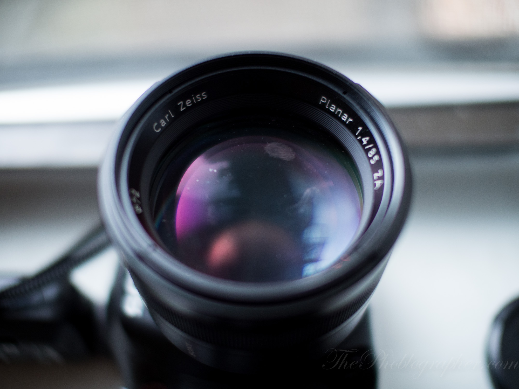 Close-up of a Carl Zeiss Planar 1.4/85 camera lens with reflections visible on the glass.