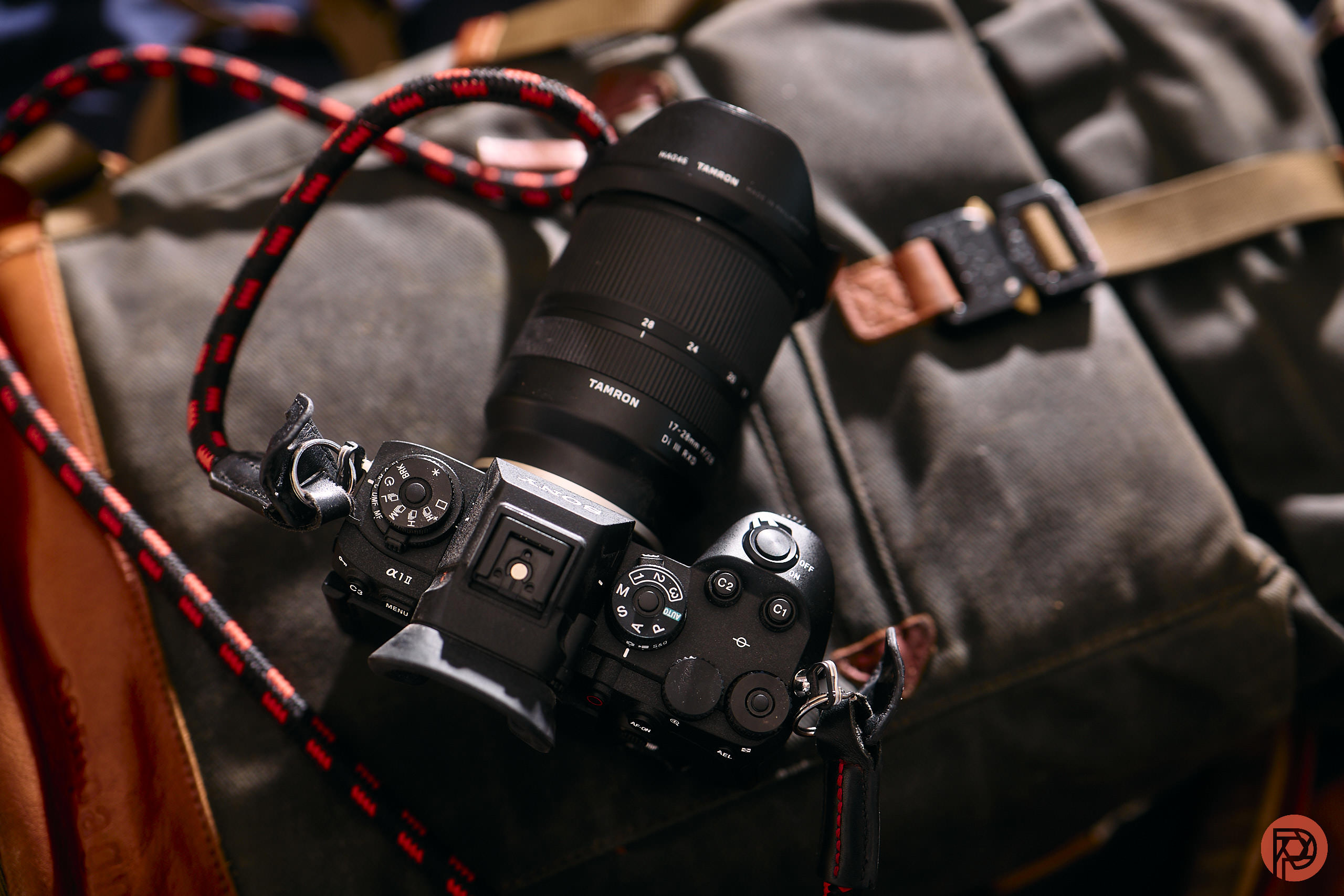A digital camera with a large lens rests on a gray backpack with brown leather straps.