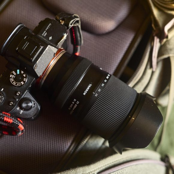A Sony camera with a Tokina lens rests on a gray camera bag with a red and black strap attached.